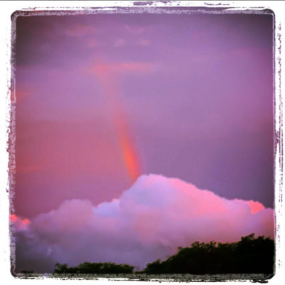 An image of a rainbow rising out of a white cloud. The whole image has a purple filter and white frame.