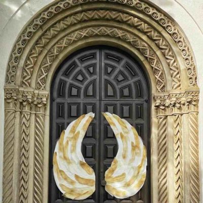 Ornate door. 3 golden arches surround a black carved wooden door. Upon the door are two golden angel wings.