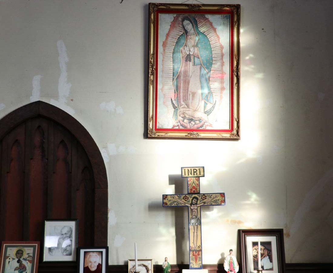 A collection of framed art and a cross against a wall with light streaming in.