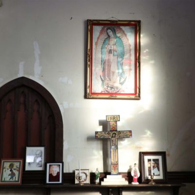 A collection of framed art and a cross against a wall with light streaming in.